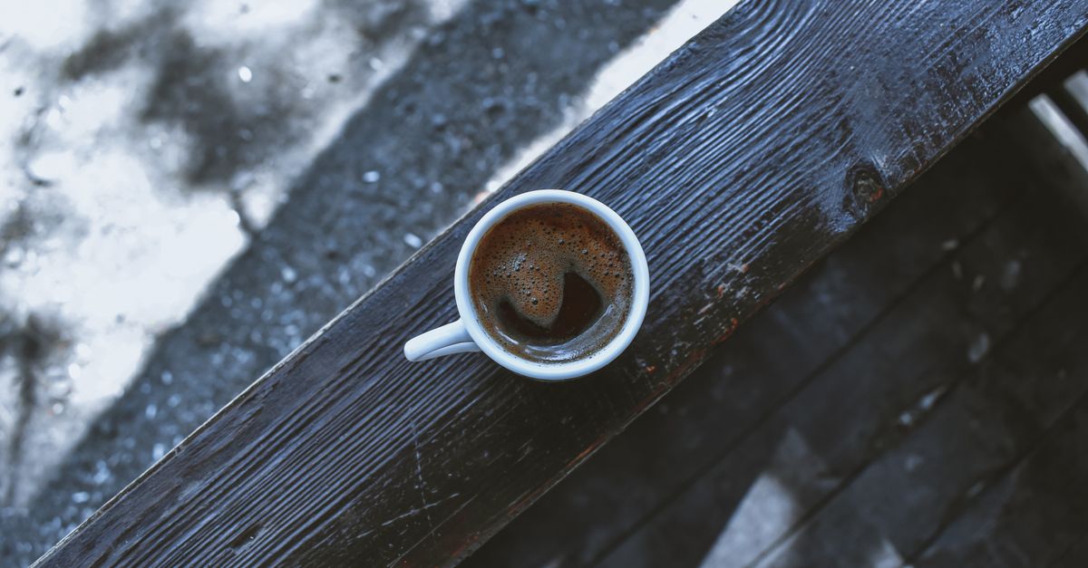 A cafe terrace with rain falling outside and a coffee cup on the table.